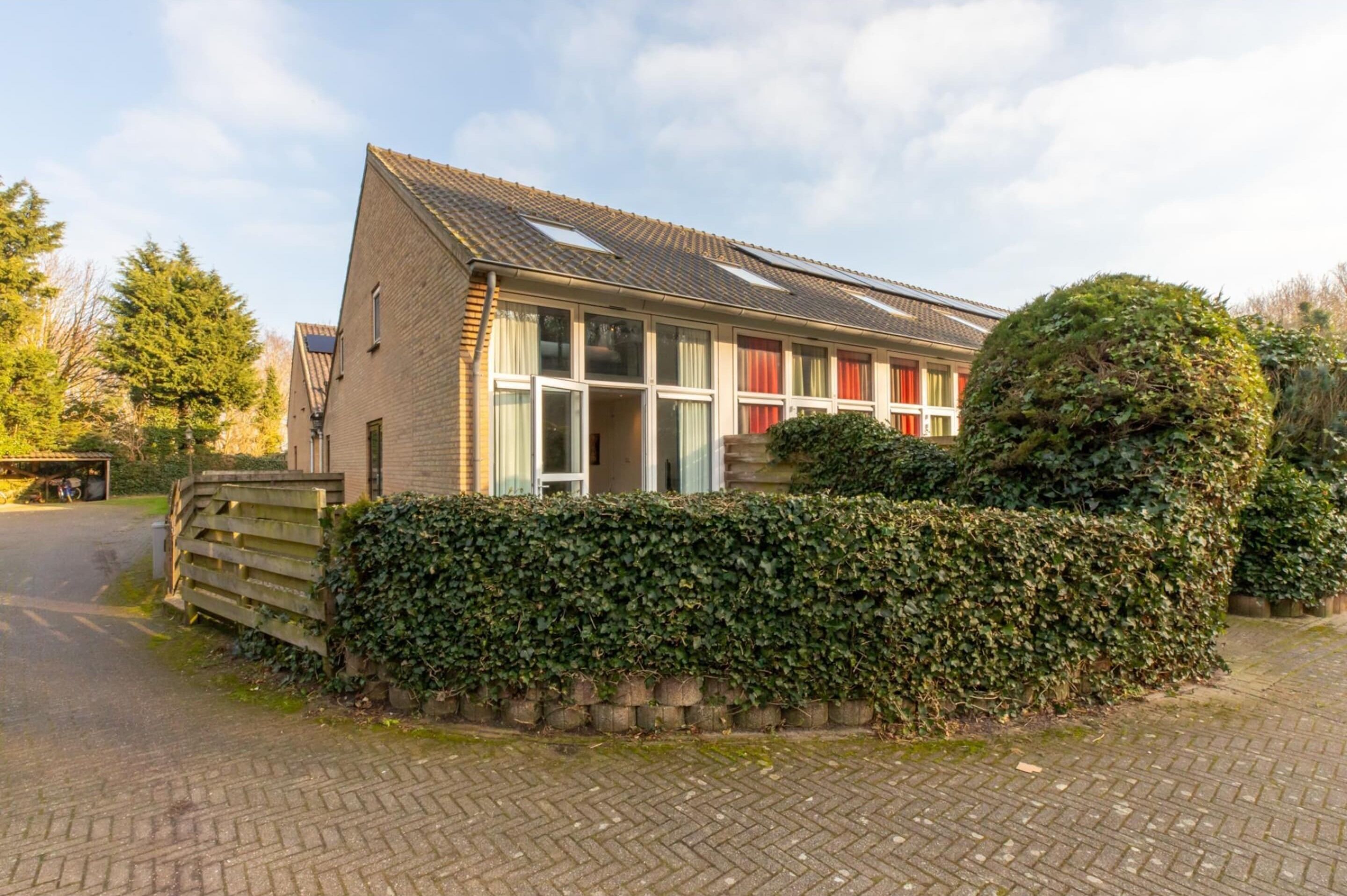 A two-story house with a tiled roof, large windows, and a well-maintained hedge.