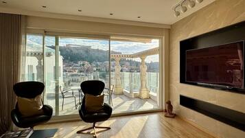 Une pièce spacieuse avec un grand balcon, un téléviseur fixé au mur et deux fauteuils modernes.