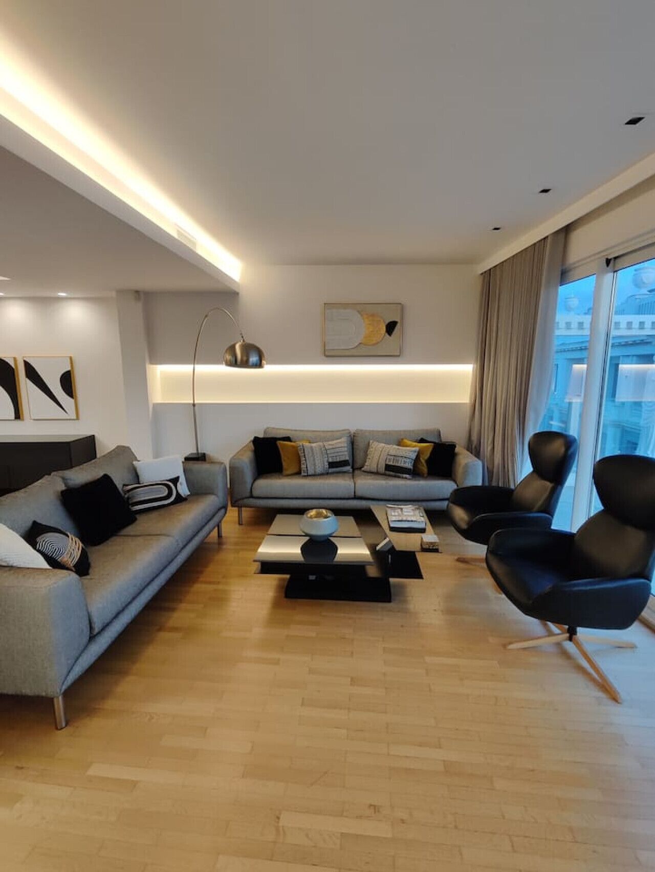 A modern living room with a grey sofa, black armchairs, and a coffee table.