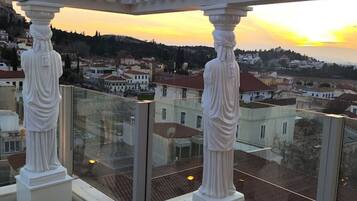 Un balcon doté de colonnes blanches et d’une balustrade en verre, offrant une vue sur le paysage urbain au coucher du soleil.