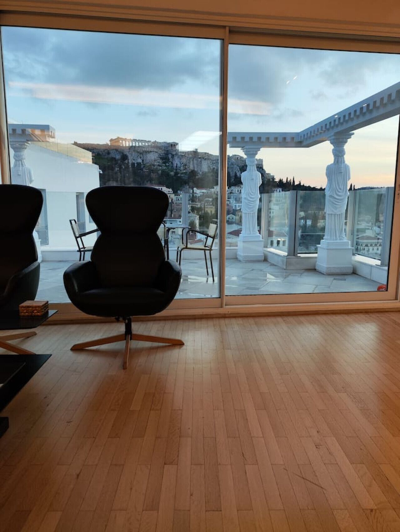 Une chambre moderne dotée d’une grande fenêtre donnant sur un paysage urbain et offrant une vue sur des ruines antiques.