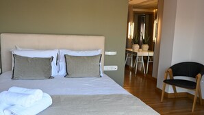 A neatly made bed with a grey duvet and two pillows, a wooden chair, and a small desk with a chair. - Luxury Acropolis-View Apartment with Panoramic Terrace | Monastiraki (Athina)