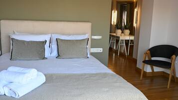 A neatly made bed with a grey duvet and two pillows, a wooden chair, and a small desk with a chair.