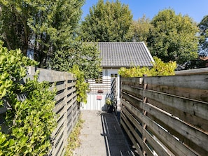 En smal stig leder fram till en byggnad med ett tak täckt av tegelpannor, omgiven av grönska och ett trästaket.