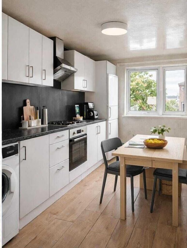 A modern kitchen with white cabinets, a black countertop, a stove, and a dining area with a table and chairs.