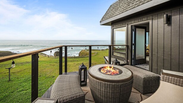 Un balcón con mobiliario de mimbre, una chimenea y vista al océano.