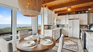 Una cocina moderna con armarios blancos, un comedor con una mesa redonda y vista al océano.