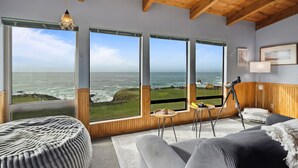 Habitación con amplios ventanales que ofrecen vistas al océano, vigas de techo de madera, un telescopio y una zona de estar acogedora.