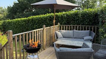 Eine Holzterrasse mit Grill, Gartenmöbeln und einer Hecke im Hintergrund.