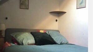 A bedroom with a bed, pillows, a wall-mounted lamp, and two framed pictures. - Studio with garden (Enchastrayes)