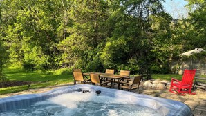 Un jacuzzi rodeado de mobiliario exterior y un exuberante jardín verde.