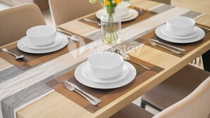 Une table à manger dressée avec de l’assiette blanche, des bols et des couverts, et un vase rempli de fleurs jaunes placé sur la table.
