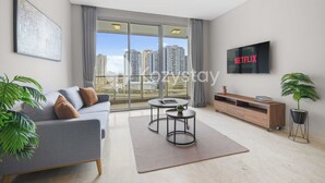 Un salon moderne avec un canapé gris, une table basse ronde, un téléviseur affichant le logo « NETFLIX » et une grande fenêtre donnant sur la ville.