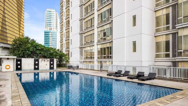 Une piscine entourée de chaises longues, elle-même bordée d’un bâtiment blanc doté de nombreuses fenêtres et de balcons.