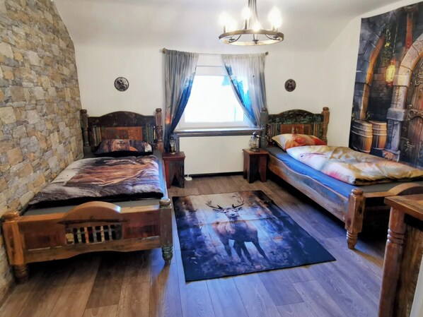 Een kamer met twee houten bedden, een stenen muur, een kroonluchter, een raam met gordijnen en een schilderij aan de muur.