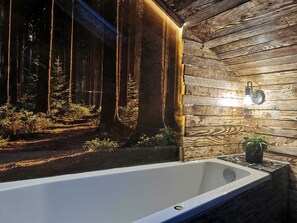 Een moderne badkamer met een badkuip, houten wandbekleding en uitzicht op een bos door een raam.