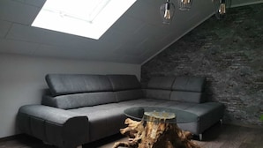 Et moderne loftværelse med en grå hjørnesofa, et sofabord i glas og en unik træstub-base.