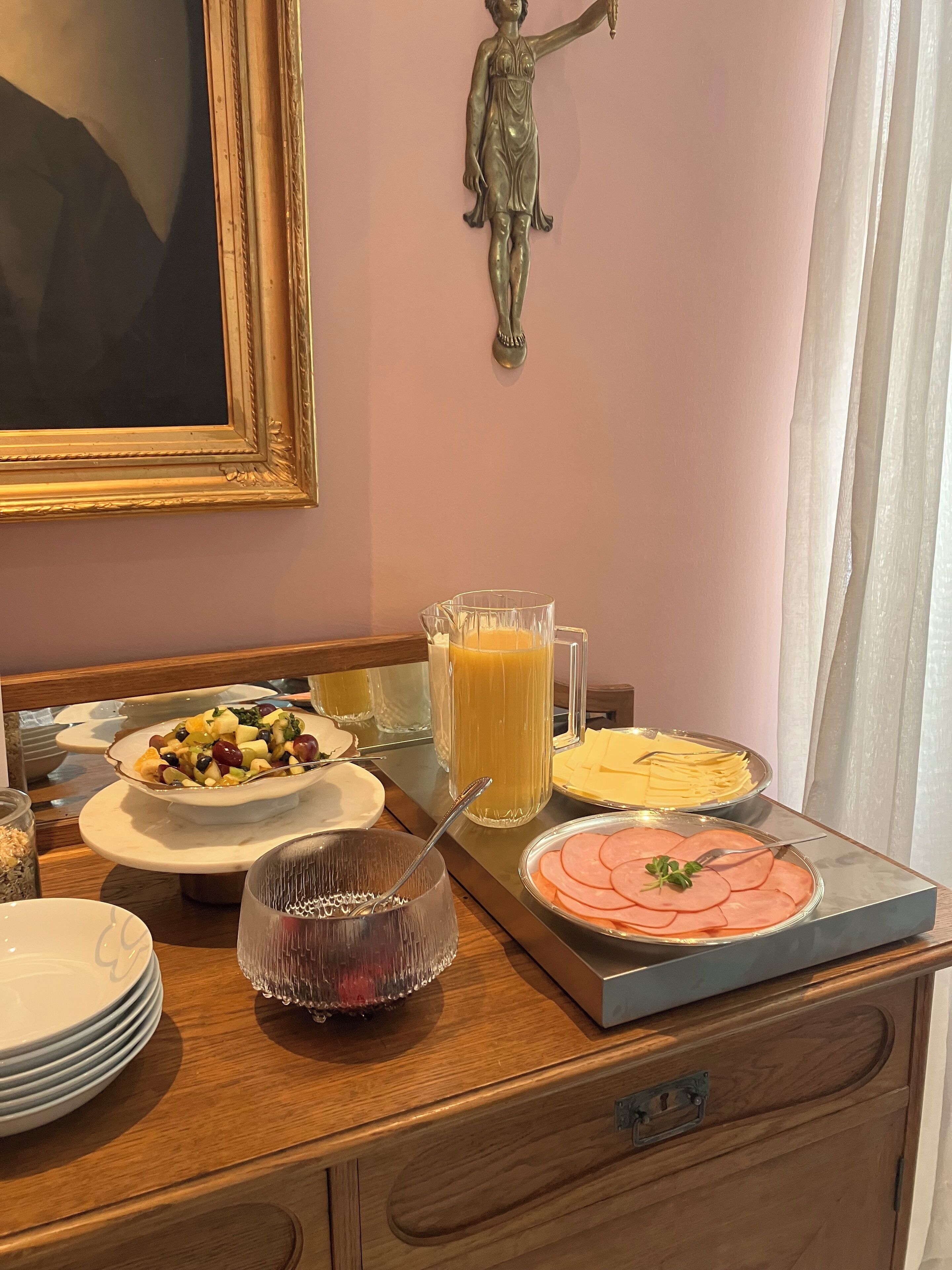 A breakfast buffet with various dishes, a glass of orange juice, and a statue on the wall.