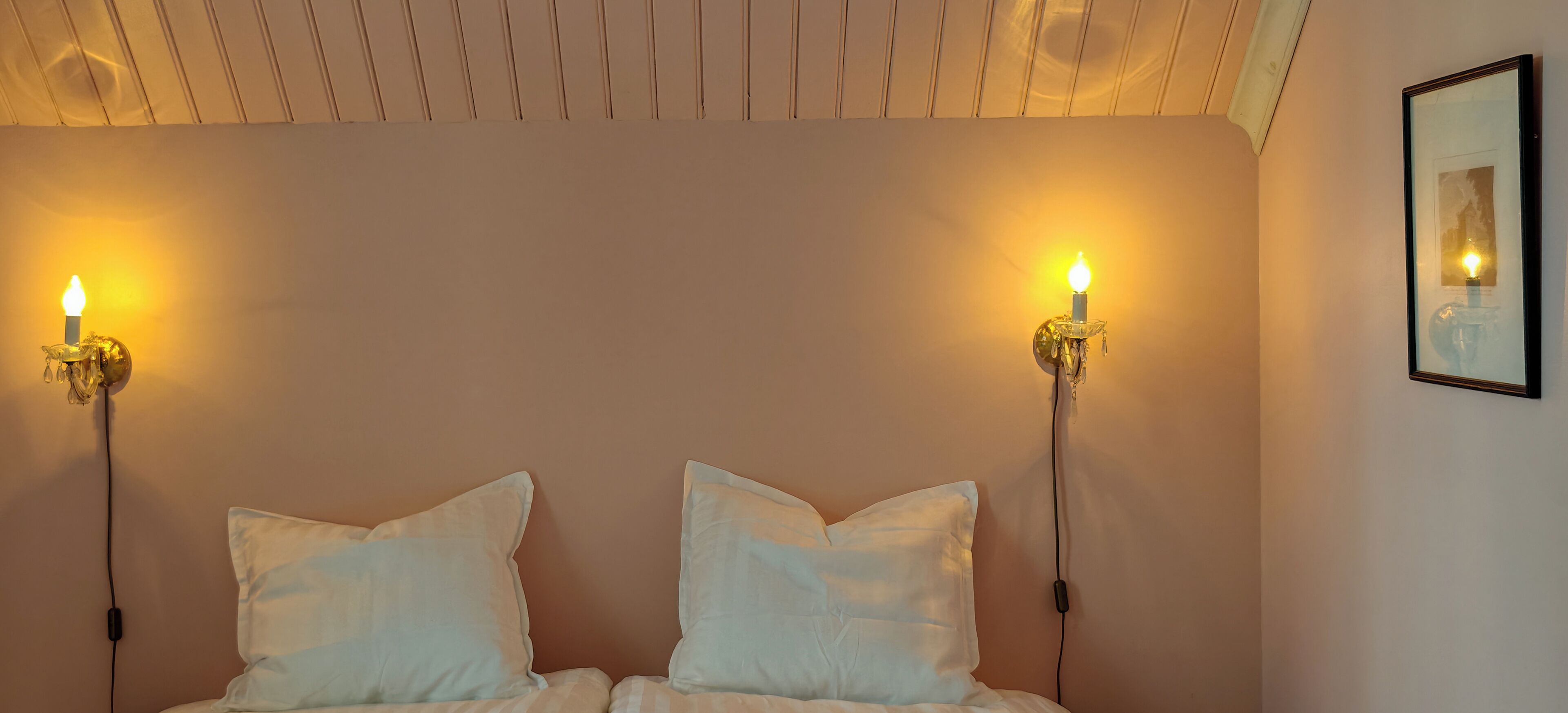 Une chambre à coucher avec deux oreillers blancs, un lit et deux lampes fixées au mur, chacune portant une bougie.