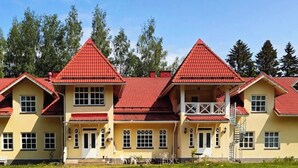A multi-story building with red-tiled roofs and yellow walls, featuring a balcony and outdoor seating area. - Wiisalan Kartano (Rantasalmi)