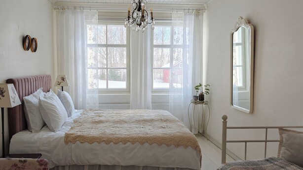 A bedroom with a bed, a chair, a lamp, a mirror, and a window with curtains. - Wiisalan Kartano (Rantasalmi)