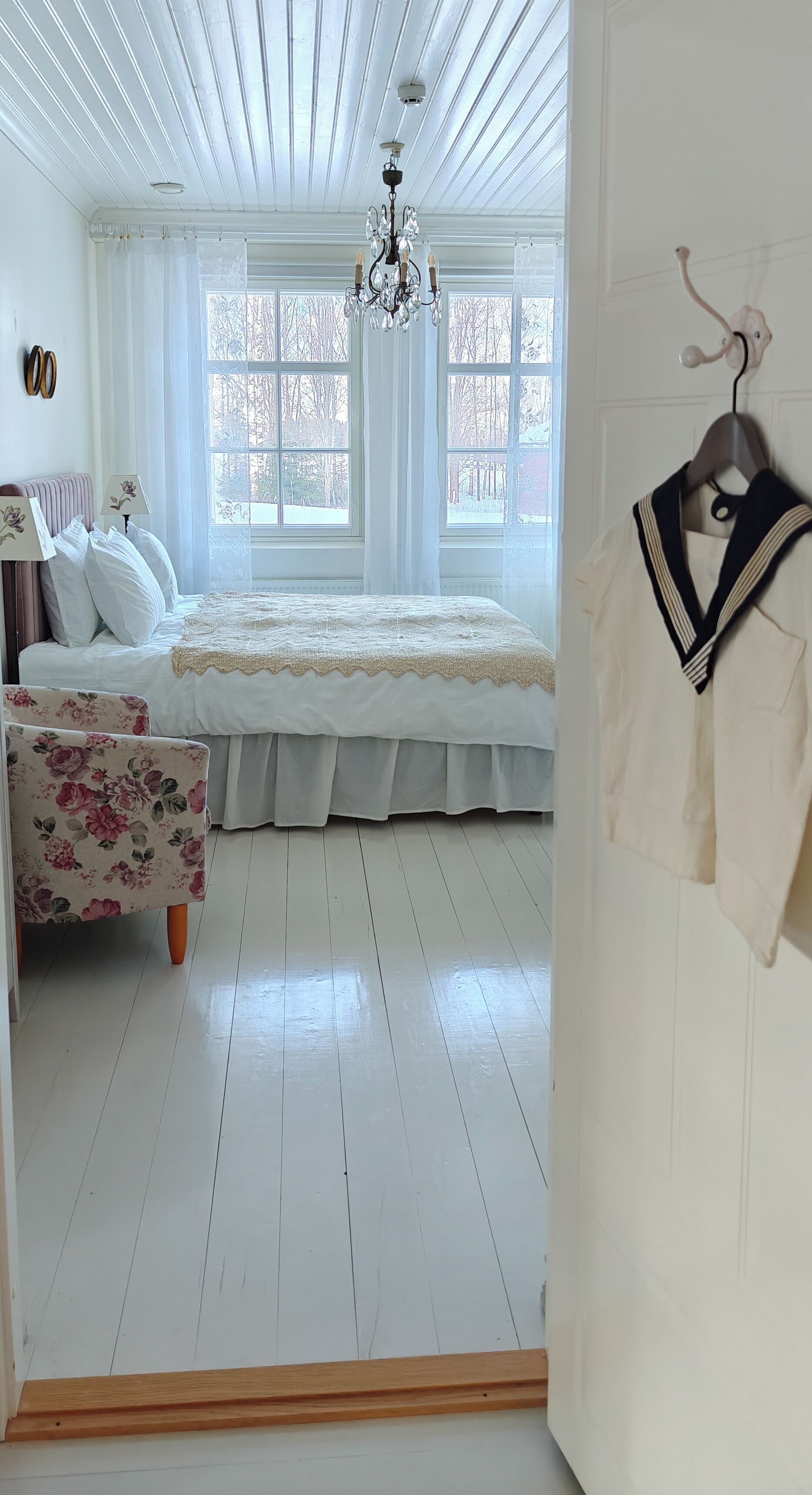 Une chambre avec un grand lit, un fauteuil à motifs floraux et un manteau suspendu.
