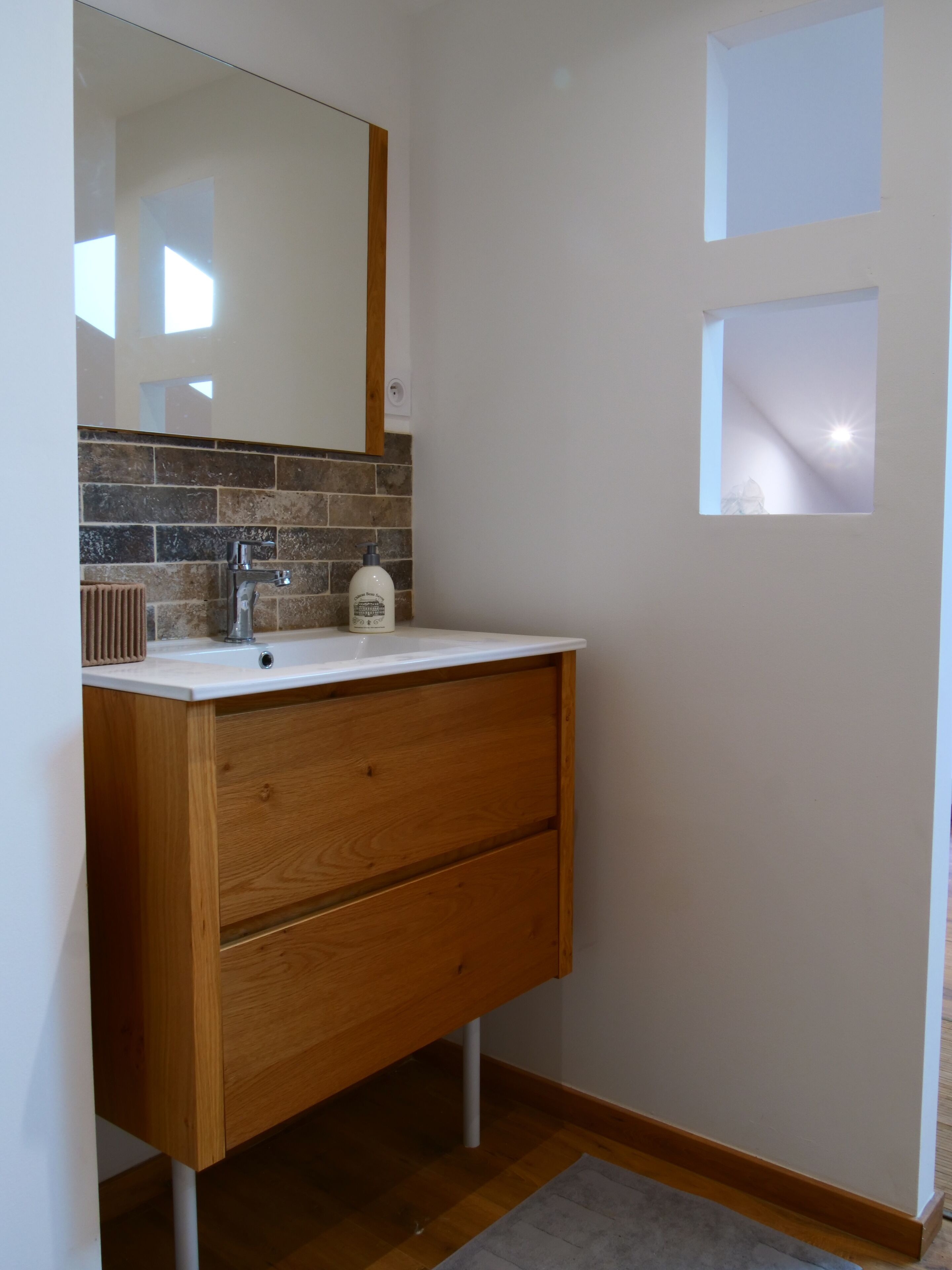 A bathroom with a wooden vanity, a white sink, and a mirror above it.