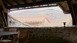 A rustic dining area with a stone wall, wooden ceiling, and a view of a hillside. - House "Les sauvages" - Nature and charm on the banks of the Allier 8 to 10 people (Blassac)