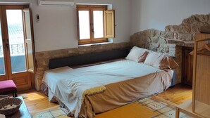 A cozy bedroom with a wooden ceiling, a stone wall, a bed with a headboard, a window, and a wardrobe.