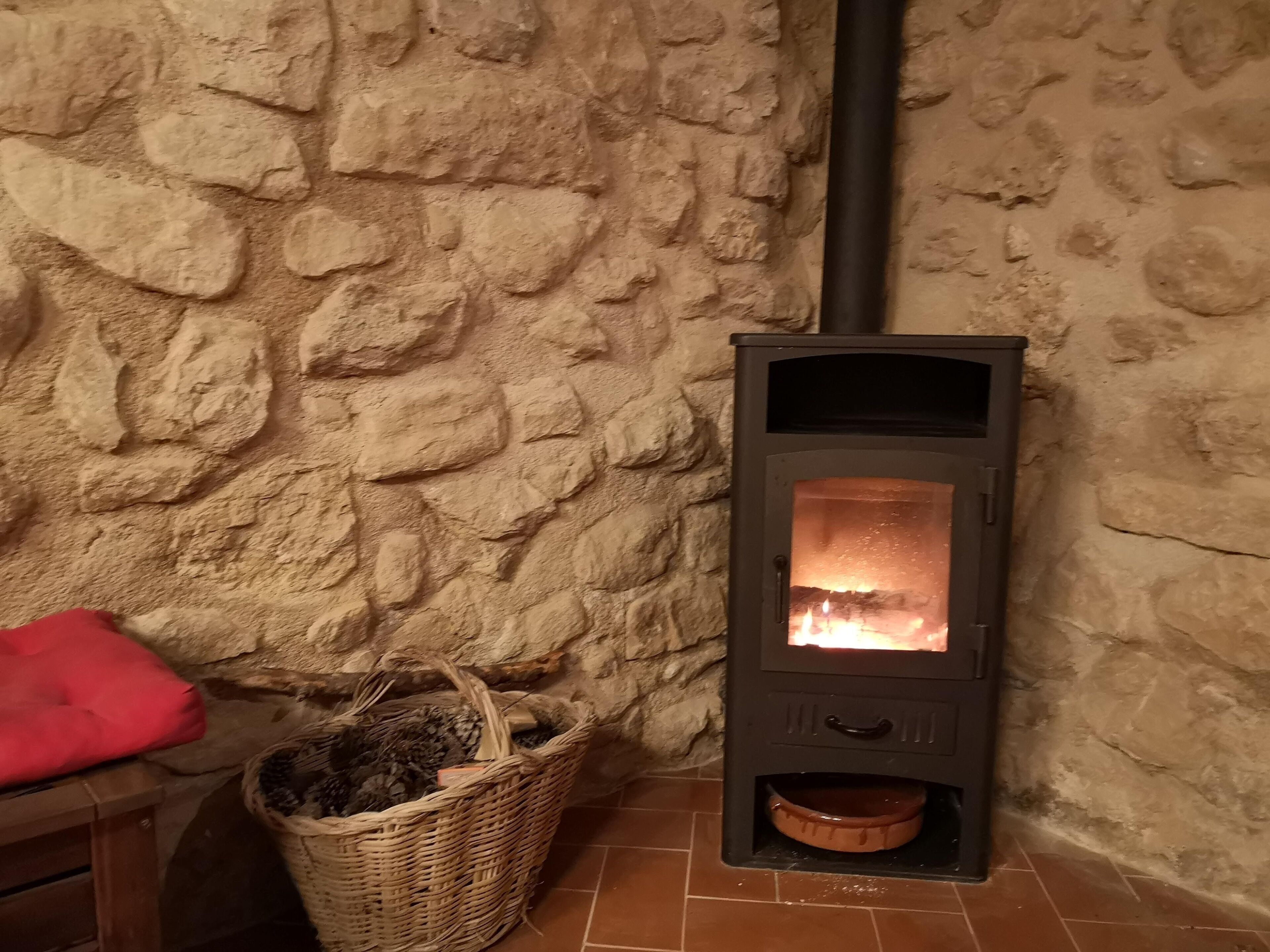 A stone wall with a wood-burning stove, a wicker basket, and a red cushion.