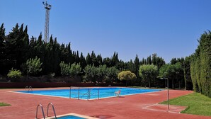 A rectangular swimming pool with a red deck, surrounded by trees and a tall communication tower.
