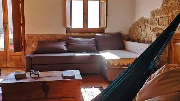 A cozy living room with a wooden ceiling, a stone wall, a sofa, a coffee table, and a hammock.