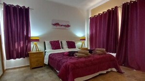 Une chambre à coucher avec un lit, des rideaux, une table de chevet et une lampe fixée au mur.