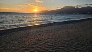 Une plage avec un coucher de soleil sur l’océan et des montagnes en arrière-plan.