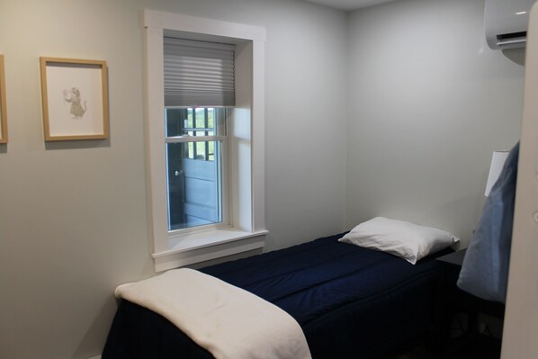 A small, neatly arranged bedroom with a single bed, a window with blinds, and a framed picture on the wall. - Sagamore Beach large group rental, steps to private beach! (Sandwich)