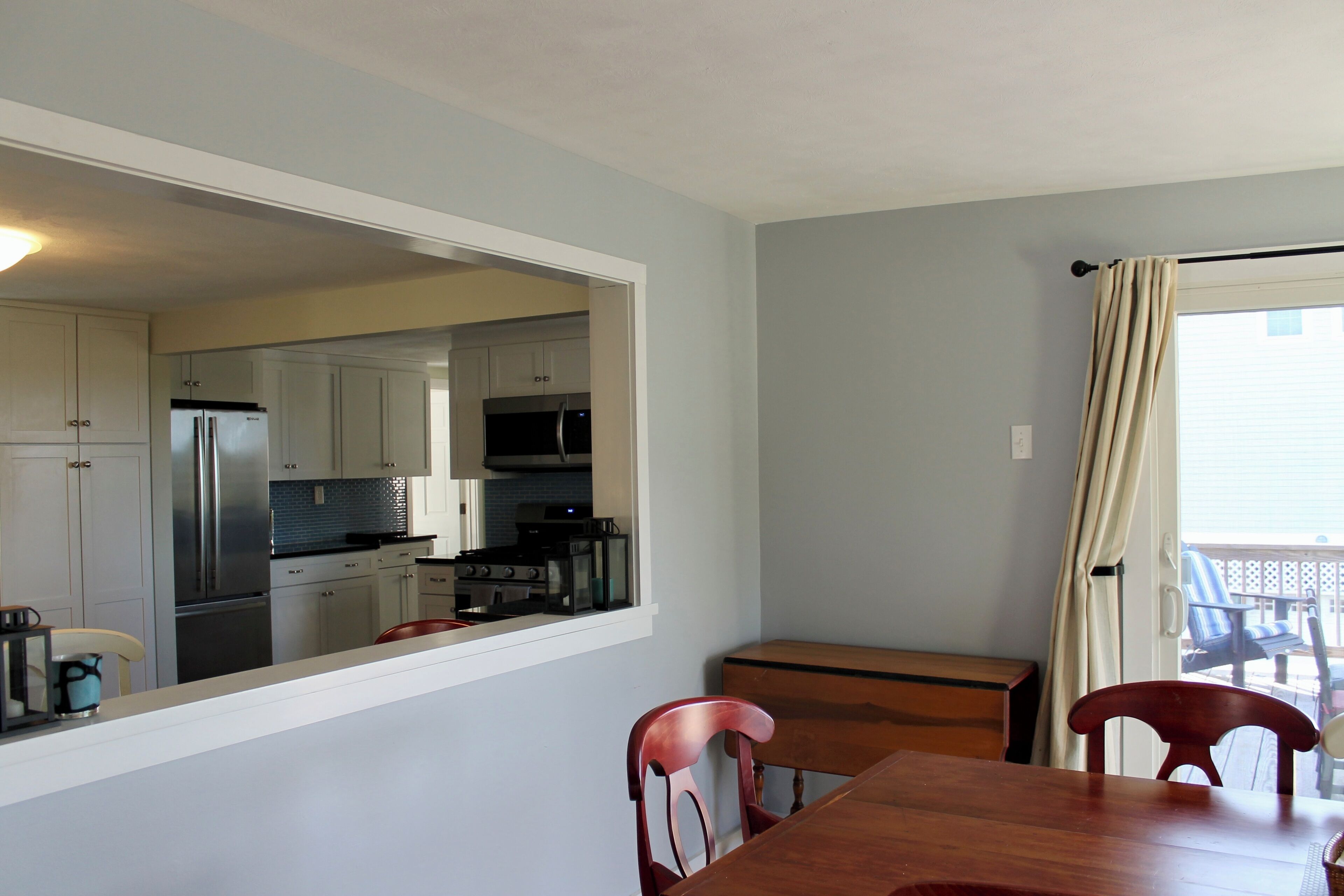 A compact kitchen with modern appliances, a dining area with a wooden table and chairs, and a view through a window to an outdoor deck.
