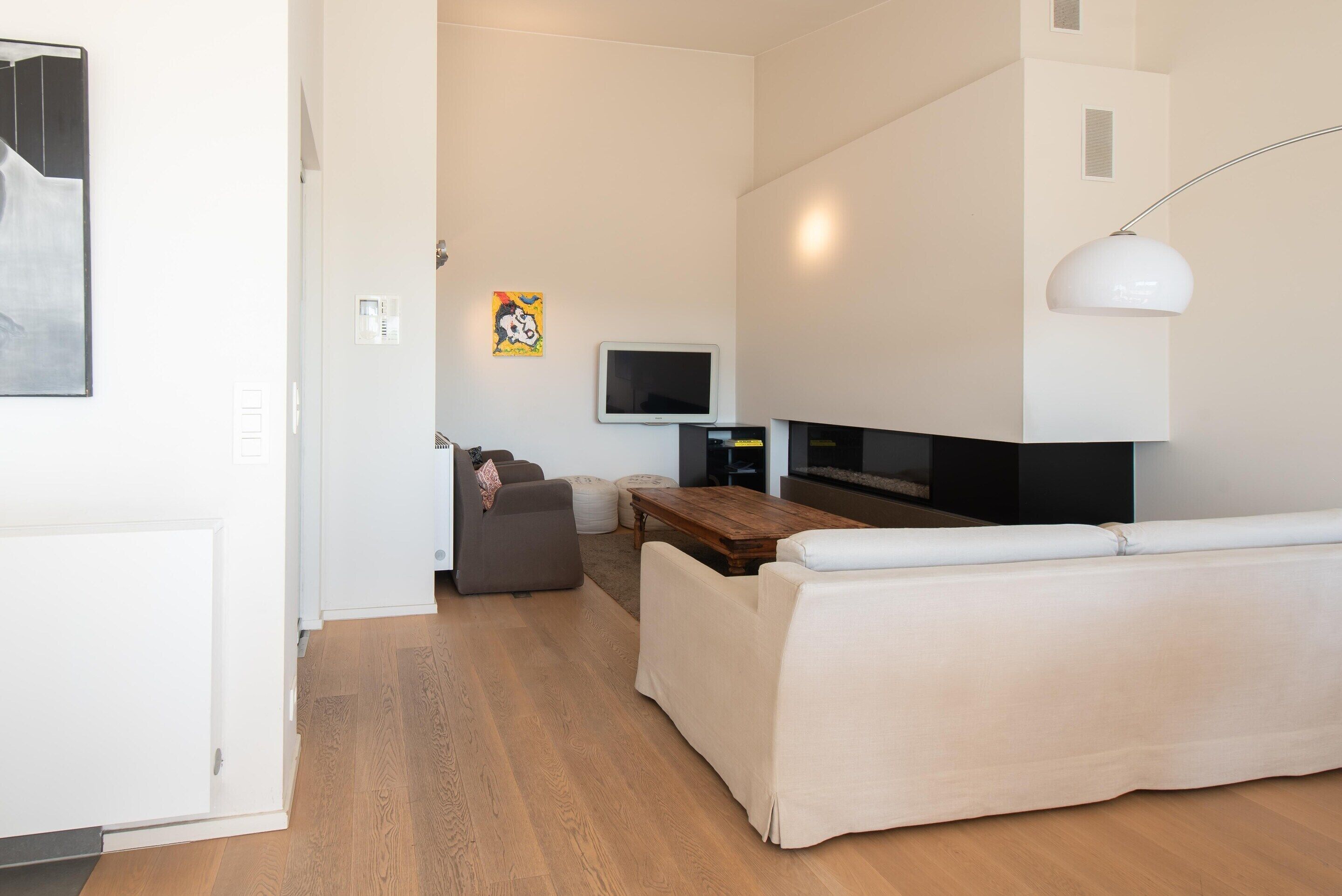 Un salon moderne avec un canapé blanc, une table basse en bois, un téléviseur à écran plat et une cheminée.
