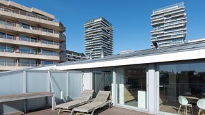 A modern building with a rooftop deck featuring wooden lounge chairs and a glass-enclosed dining area. - Central Flat With Sunny Terrace (Ostend)