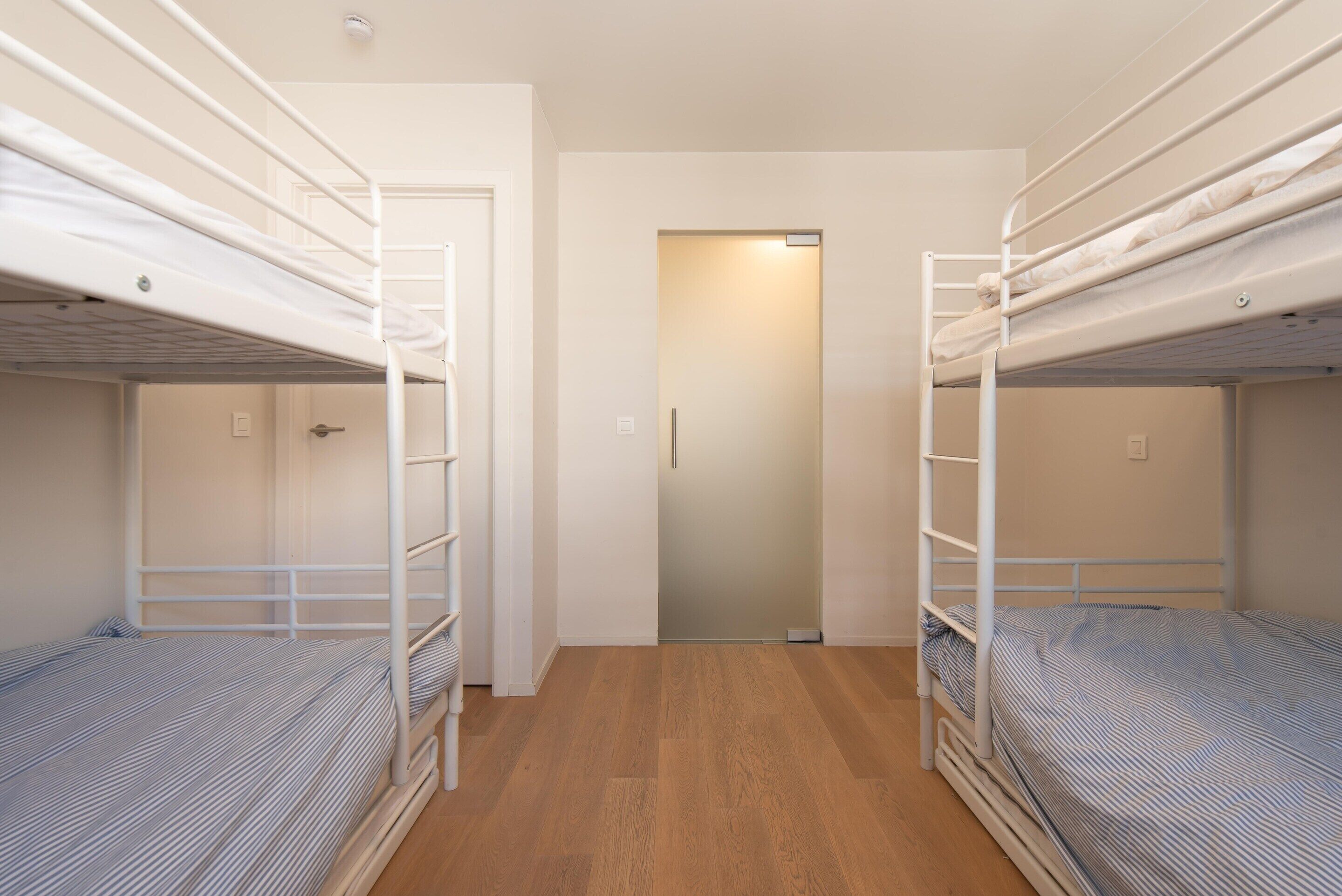 Une pièce avec deux lits superposés, un plancher en bois et une porte donnant sur une autre pièce.