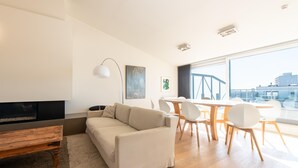 A modern living room with a sofa, a wooden coffee table, and a dining area with chairs and a table. - Central Flat With Sunny Terrace (Ostend)