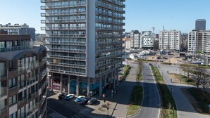 A modern high-rise building with multiple floors, surrounded by other buildings and a clear sky. - Central Flat With Sunny Terrace (Ostend)
