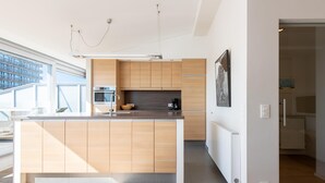 A modern kitchen with wooden cabinets, a central island, and a large window providing natural light. - Central Flat With Sunny Terrace (Ostend)