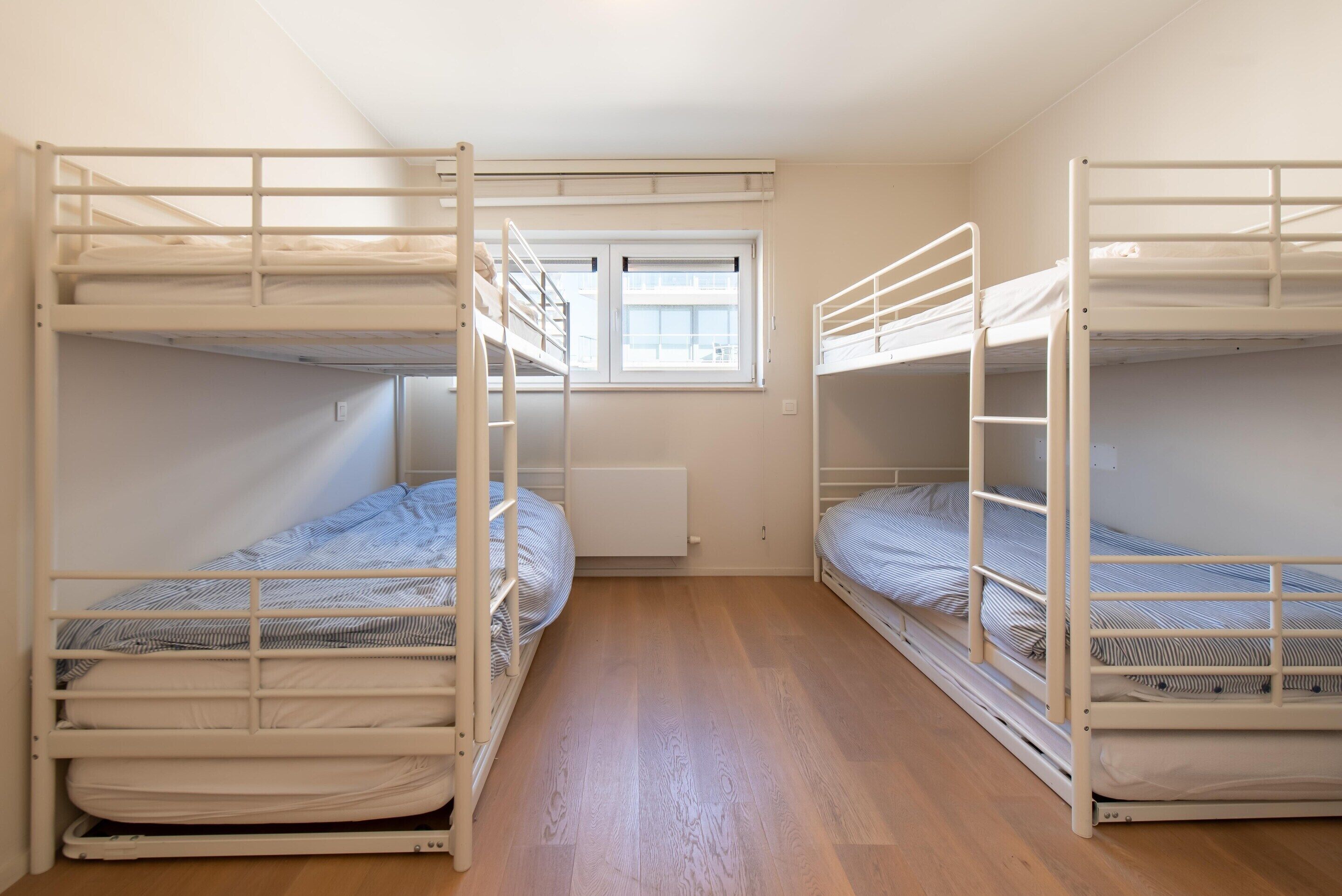 Een studentenkamer met twee stapelbedden, een raam en een radiator.