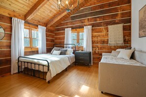 A log cabin bedroom with a bed, dresser, and sofa.
