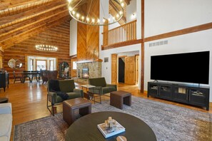 A spacious living room with a high ceiling, wooden beams, a fireplace, a large TV, and comfortable seating. - Lodge at Wildcat Hollow | Game Room, Hot Tub (Rockbridge)
