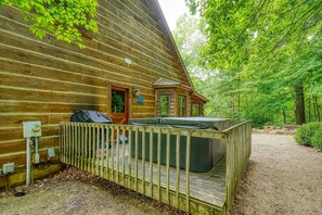 Eine Holzjagdhütte mit Whirlpool auf einer Terrasse, umgeben von einem Wald.