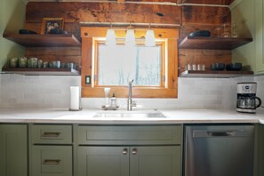 A kitchen with a window, wooden shelves, a coffee maker, and a dishwasher.