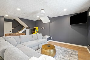 Ein modernes Wohnzimmer mit einem grauen Ecksofa, einem runden Holztisch und einem Wand-Fernseher.