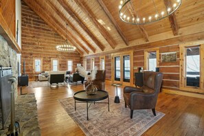 A spacious log cabin interior with a high ceiling, wooden beams, a fireplace, a stone wall, and a cozy seating area. - Lodge at Wildcat Hollow | Game Room, Hot Tub (Rockbridge)