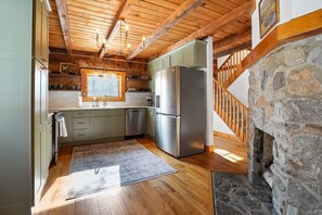 A kitchen with wooden beams, a stone fireplace, and a stainless steel refrigerator.